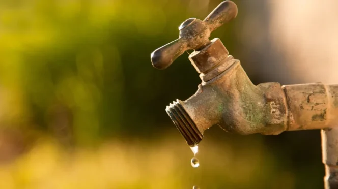 Rusty outdoor faucet dripping water drops, warm sunset background