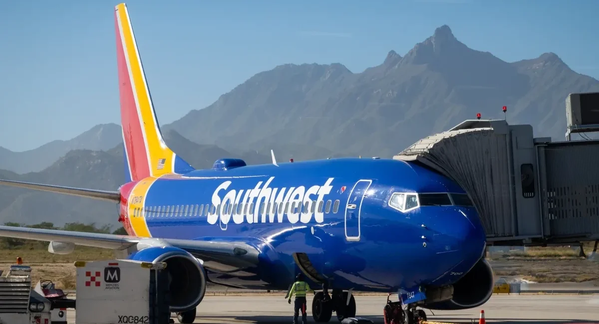 Southwest Airlines jet at gate with jet bridge attached, blue fuselage and mountainous desert backdrop