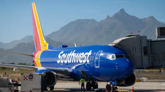 Southwest Airlines jet at gate with jet bridge attached, blue fuselage and mountainous desert backdrop