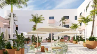 Historic Hotel Perla Reopens as Hilton Property - Gringo Gazette Sunlit hotel courtyard with white buildings, palm trees, and outdoor seating under large umbrellas.