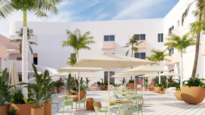 Sunlit hotel courtyard with white buildings, palm trees, and outdoor seating under large umbrellas.