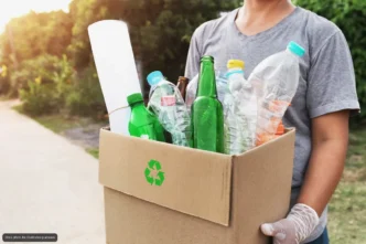 Person in a gray shirt holds a cardboard box full of recyclable plastic bottles for recycling.