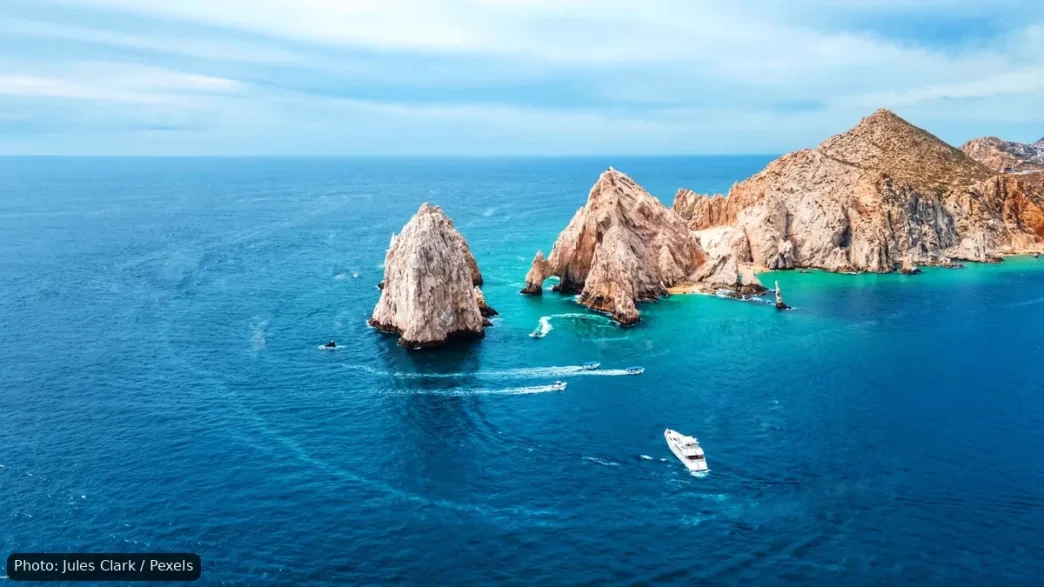 Aerial view of turquoise water surrounding jagged rocky islets with a small white boat cruising nearby.