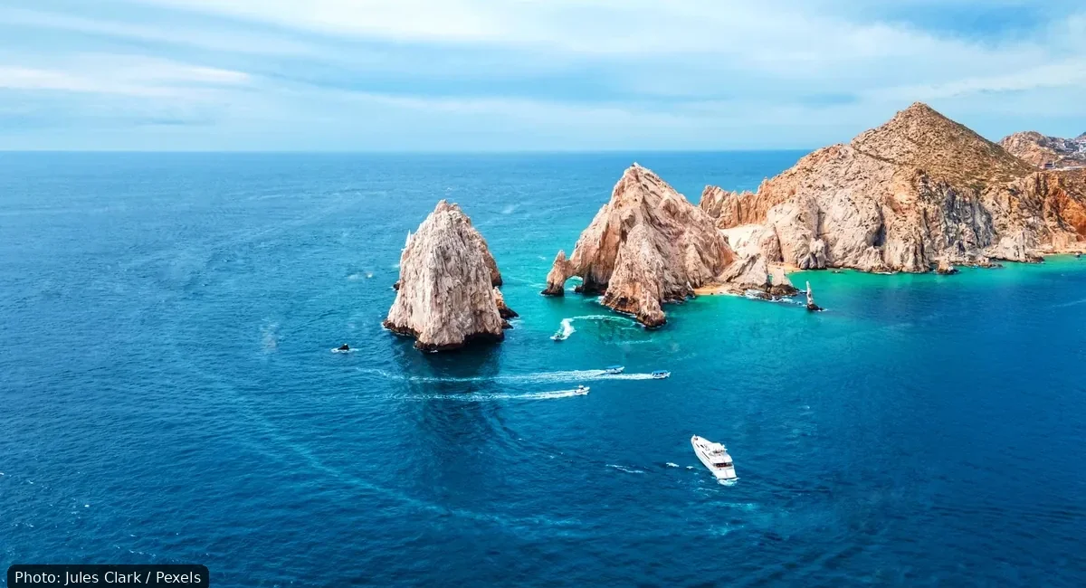 Aerial view of turquoise water surrounding jagged rocky islets with a small white boat cruising nearby.