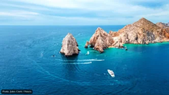 Aerial view of turquoise water surrounding jagged rocky islets with a small white boat cruising nearby.