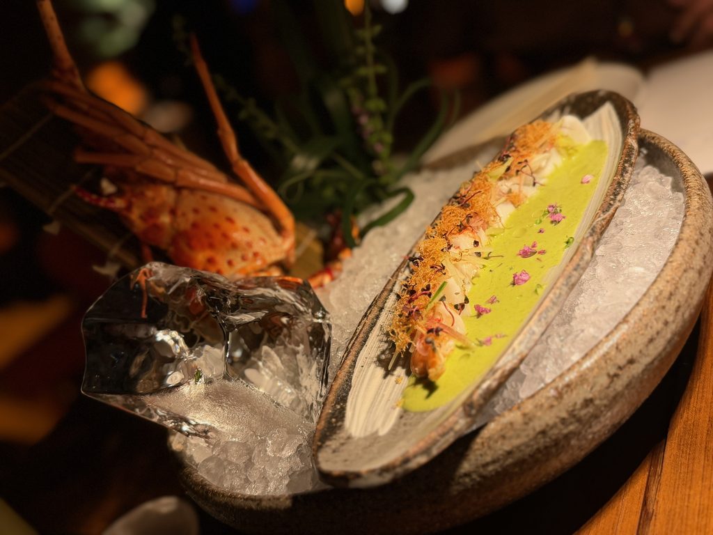 IMG_5553 - Gringo Gazette Seafood platter on ice with a lobster tail, a bright green herb sauce, and foil-wrapped items nearby on a ceramic tray