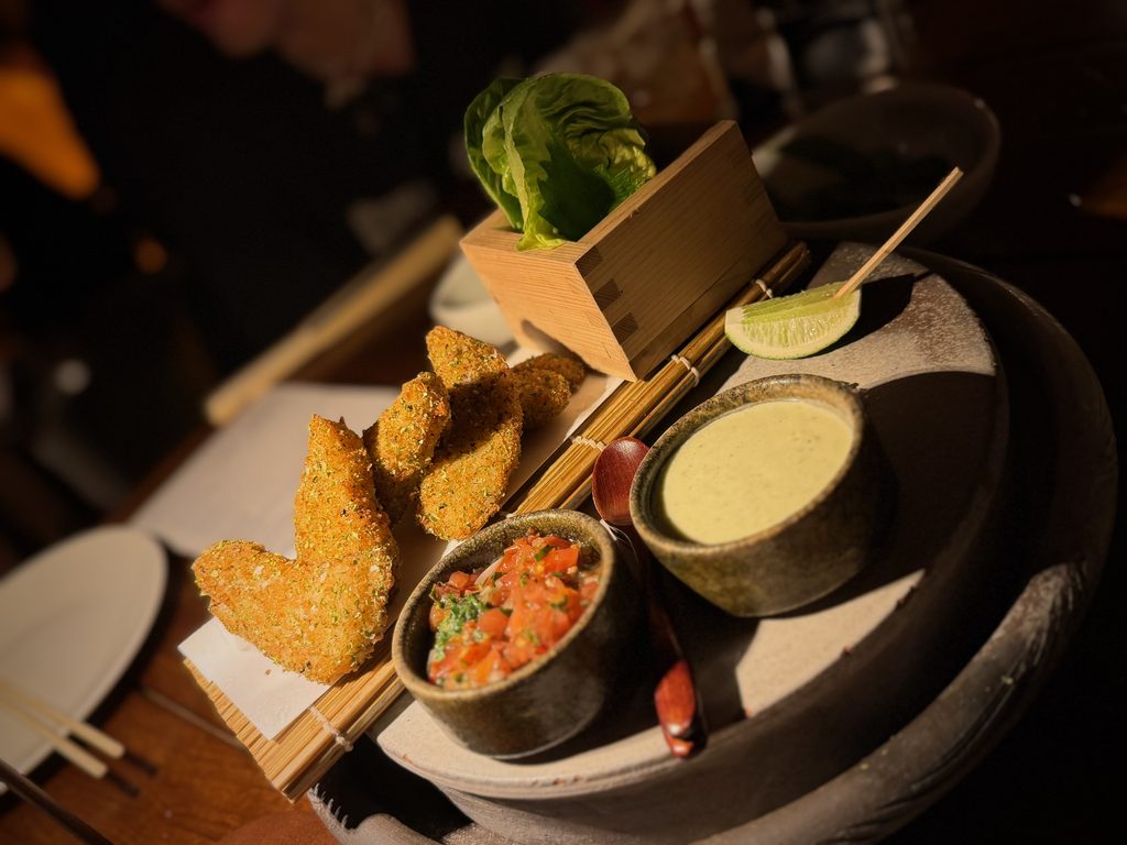 IMG_5567 - Gringo Gazette Assorted fried appetizers on a long platter with lime wedges and dipping sauces on a dark table.