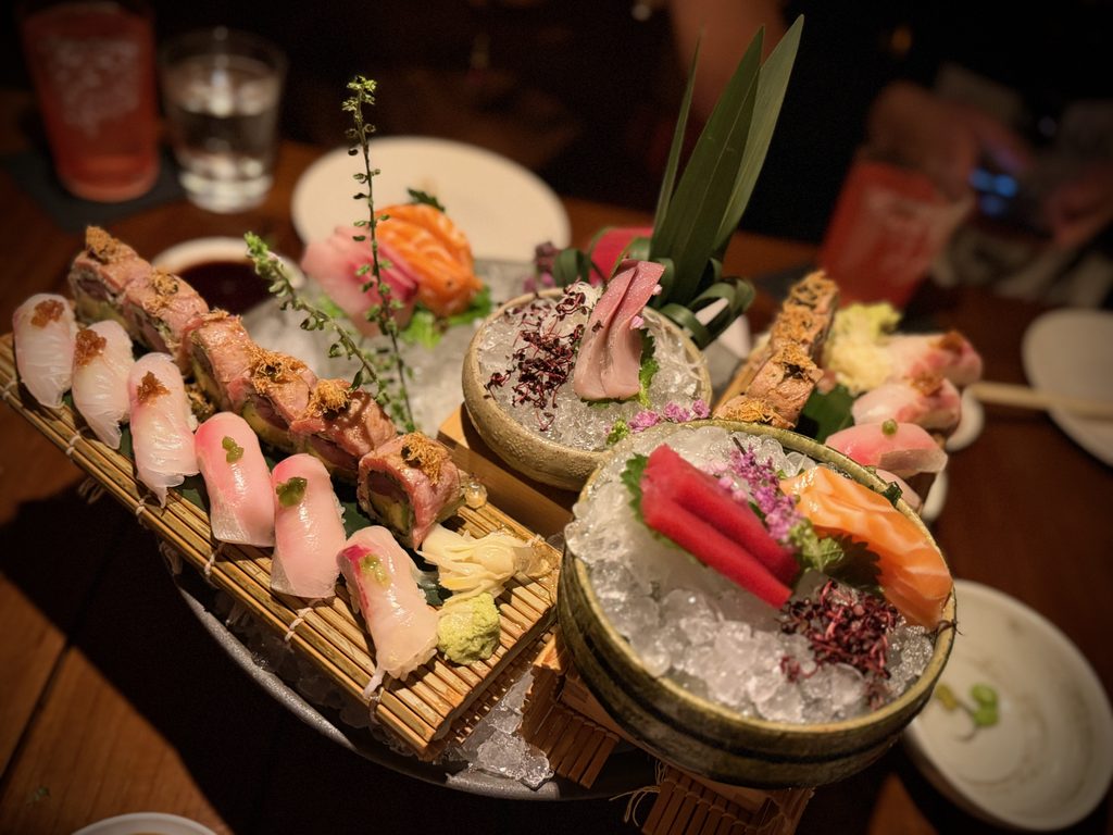 IMG_5577 - Gringo Gazette Assorted sushi and sashimi on ice, arranged on wooden and ceramic platters with wasabi and greens for garnish.