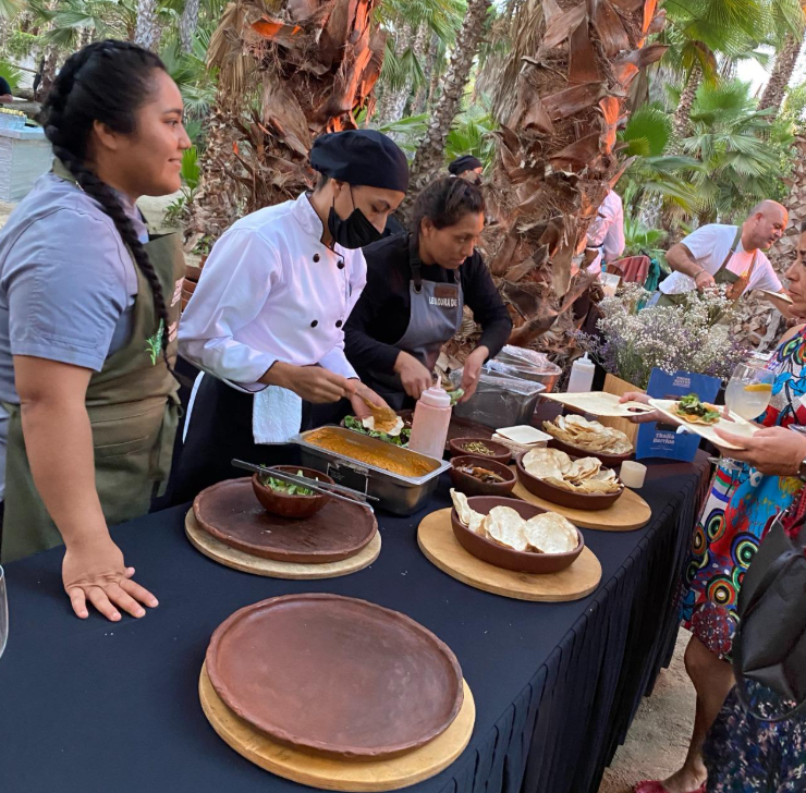 Culfantry: Chefs in white jackets serving dishes at an outdoor palm-tree food stall while guests line up for plates.
