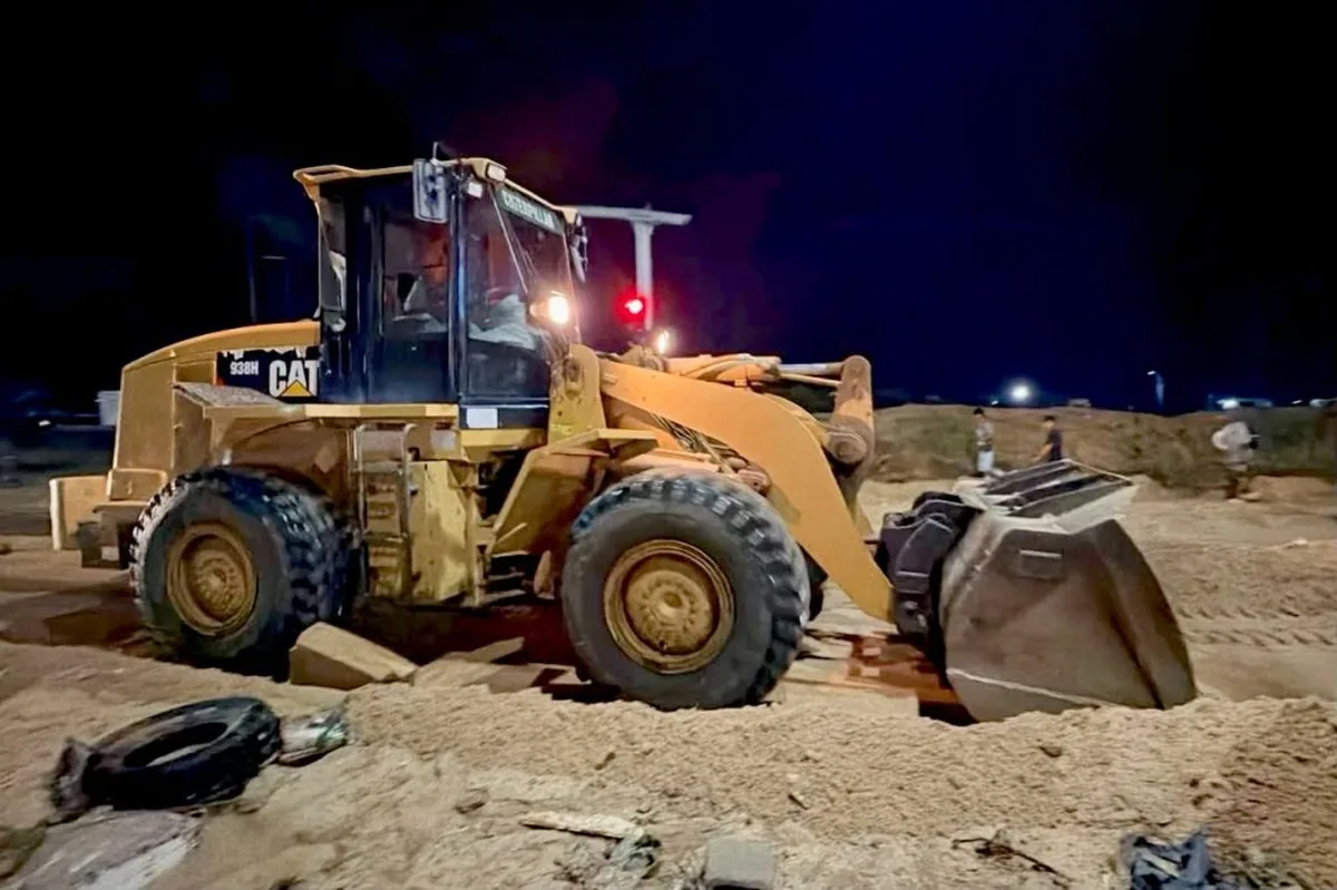 Nighttime construction scene with a large yellow CAT wheel loader and front bucket on a dirt site; debris and scattered tires in foreground.