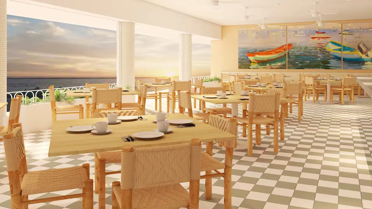 Bright seaside restaurant with wooden tables and woven chairs, checkered floor, and large windows showing a sunset view.