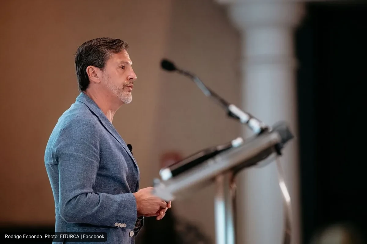 Male speaker in a blue blazer delivering a talk at a podium with a microphone on stage.
