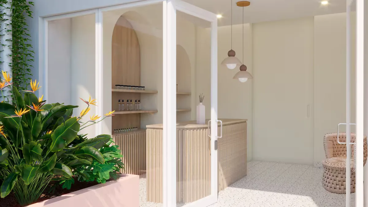 Glass-enclosed modern cafe or reception space with a wooden bar, shelves, and hanging pendant lights, flanked by lush tropical plants on the left.